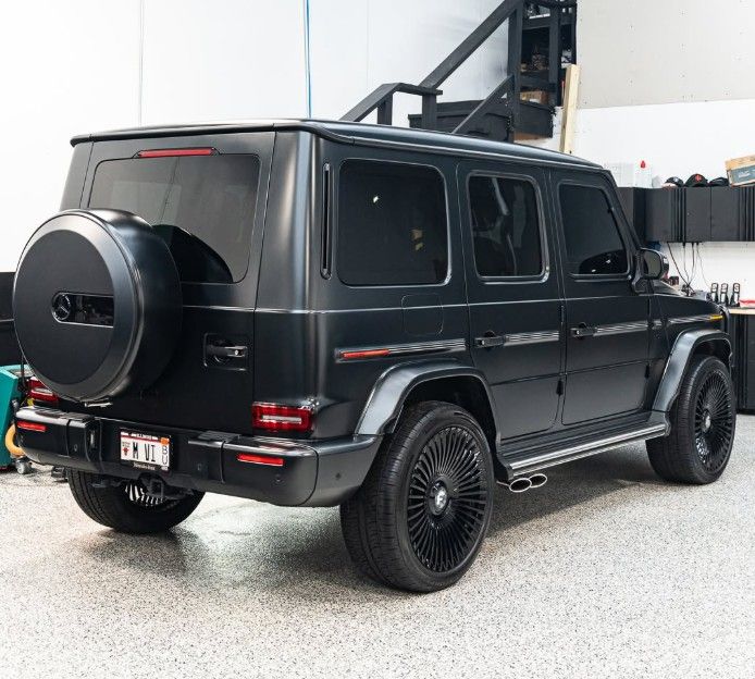Black Mercedes G-Class SUV parked indoors, rear three-quarter view with spare tire and dark tinted windows