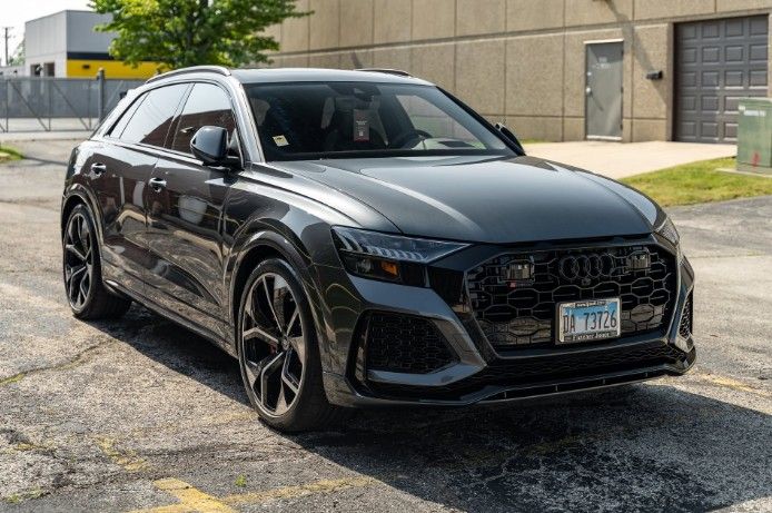 Black Audi wagon parked outdoors on a gravel lot beside an industrial building.