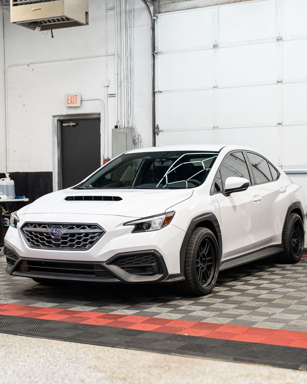 White sports sedan with black wheels parked indoors on a checkered floor.