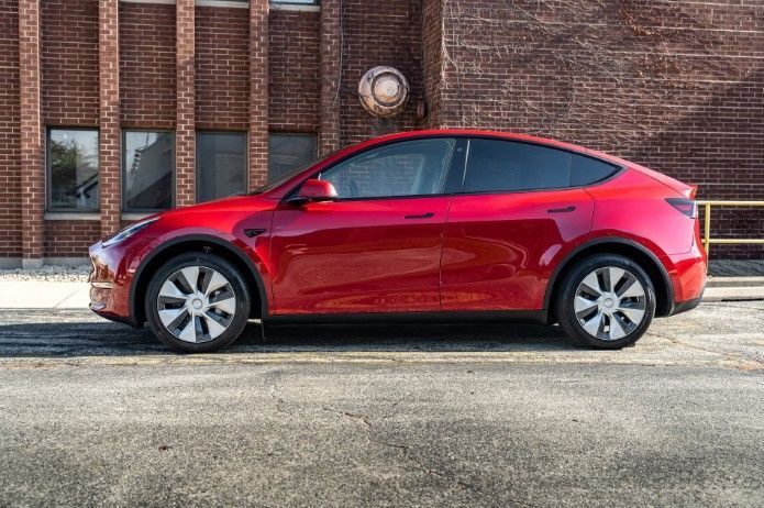 Red sedan parked beside a brick building with a clock on the wall