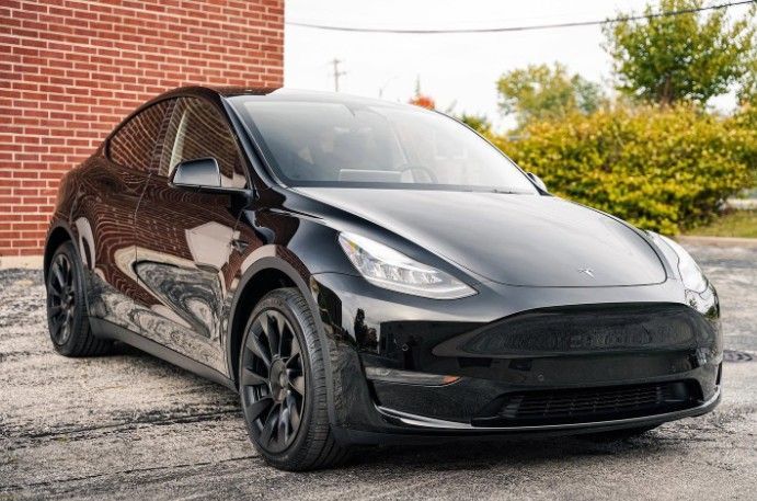 Black Tesla Model Y parked outdoors near a brick wall and trees.