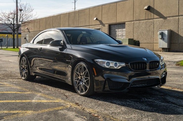 Black BMW coupe parked in a lot beside a beige building on a sunny day