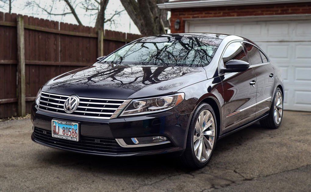 Dark blue Volkswagen CC sedan parked in front of a garage, reflecting the surroundings.