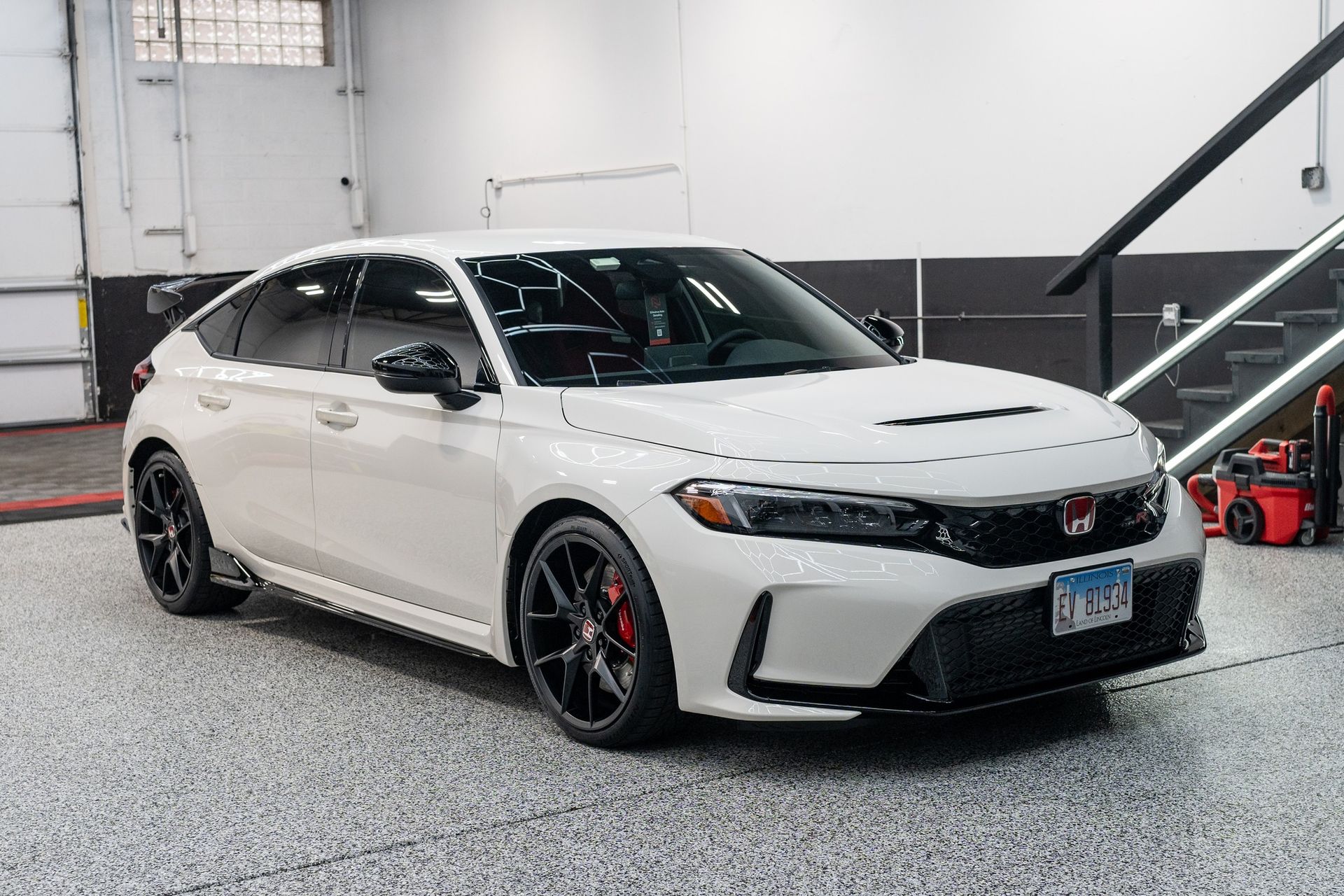 White Honda sedan with black wheels parked in a garage near a staircase
