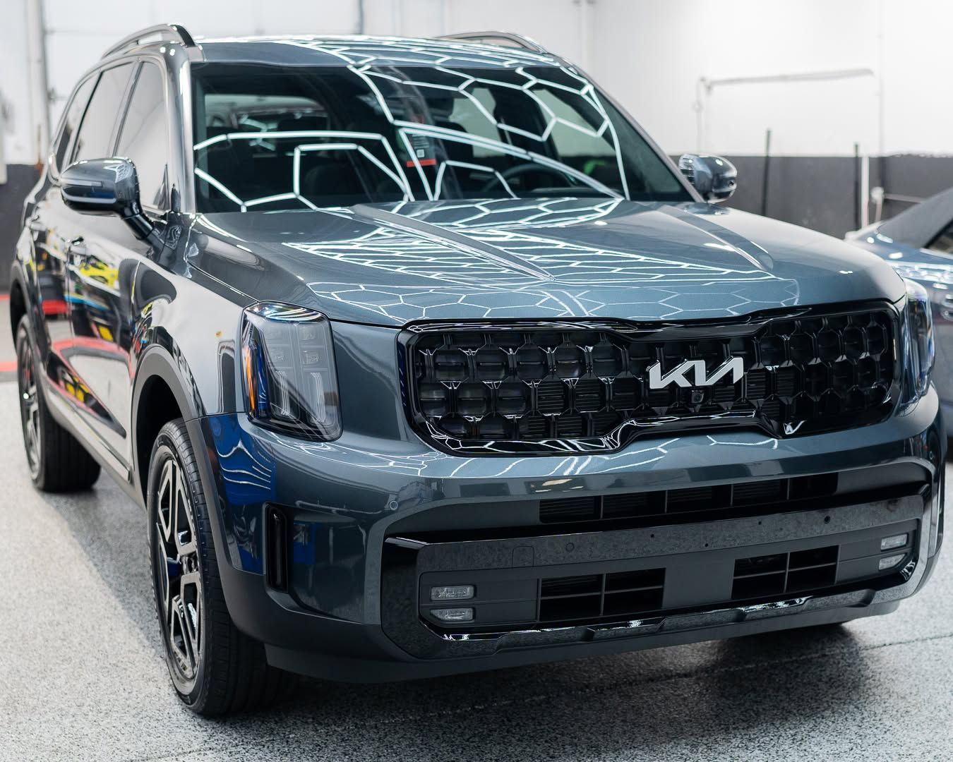Dark gray Kia SUV in a showroom, front view under bright lights