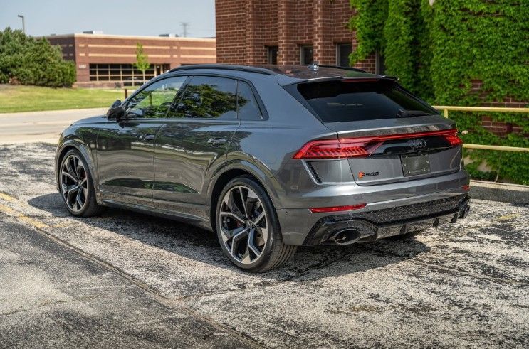 Dark gray SUV parked on a paved lot beside a brick building and green bushes