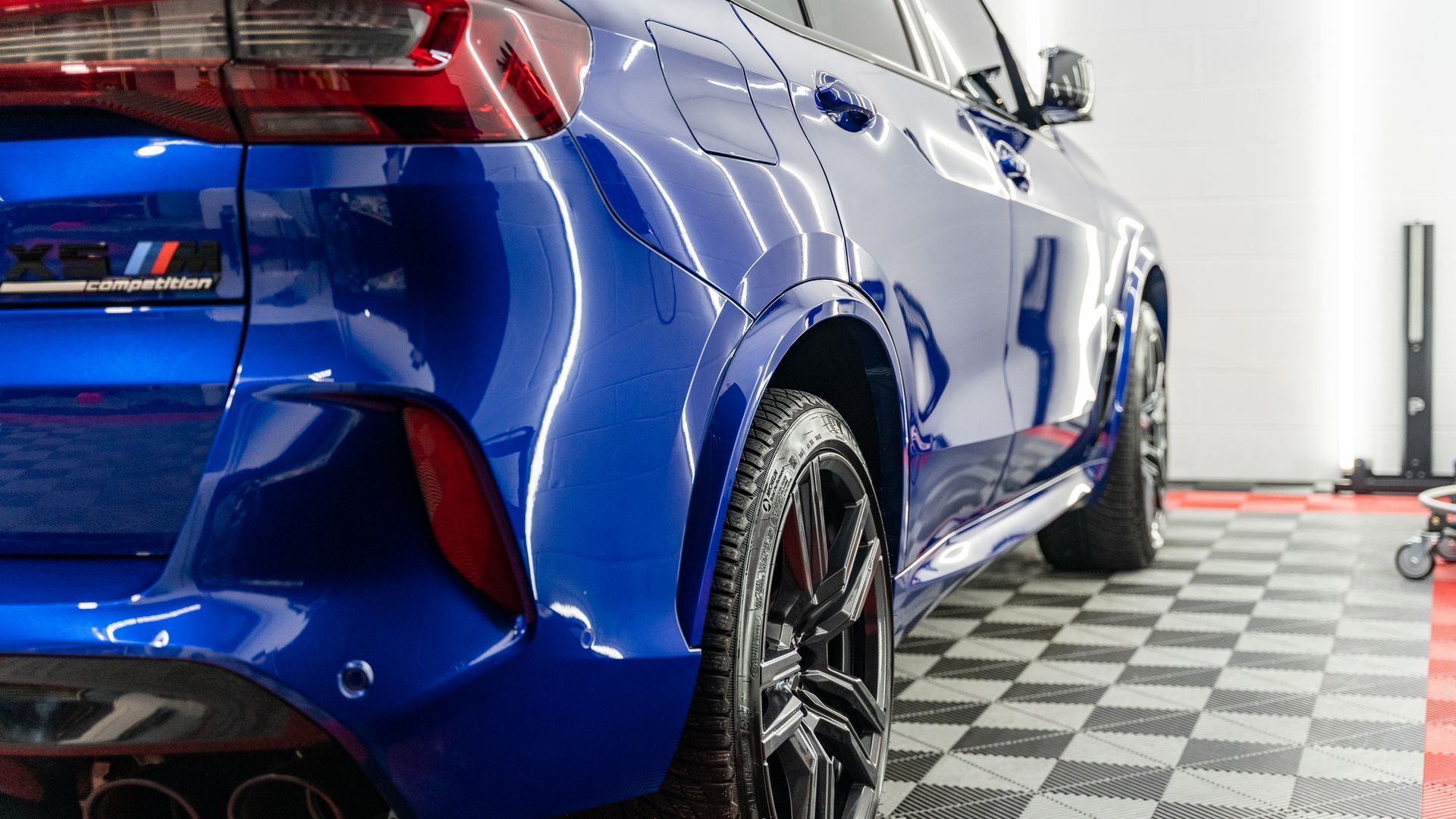 A blue car is parked on a checkered floor in a garage.
