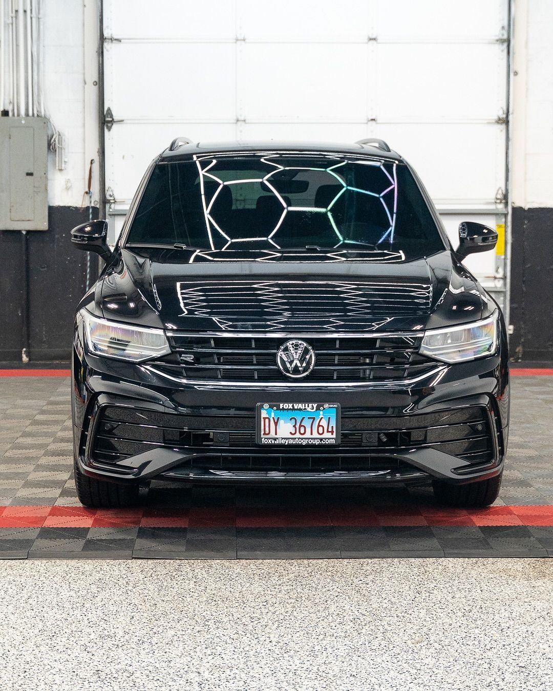Black Volkswagen SUV parked indoors in front of a white garage door, with a colorful hexagon display in the windshield