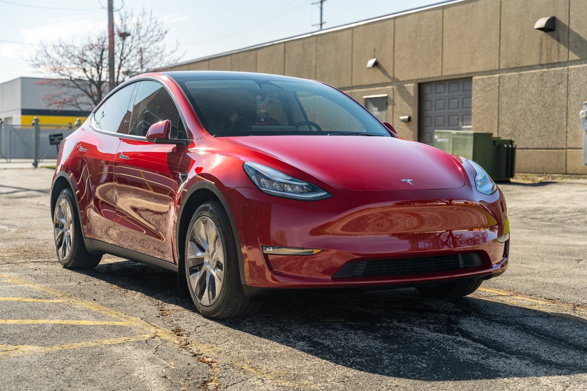 Red Tesla sedan parked outdoors on a gravel lot beside a beige building