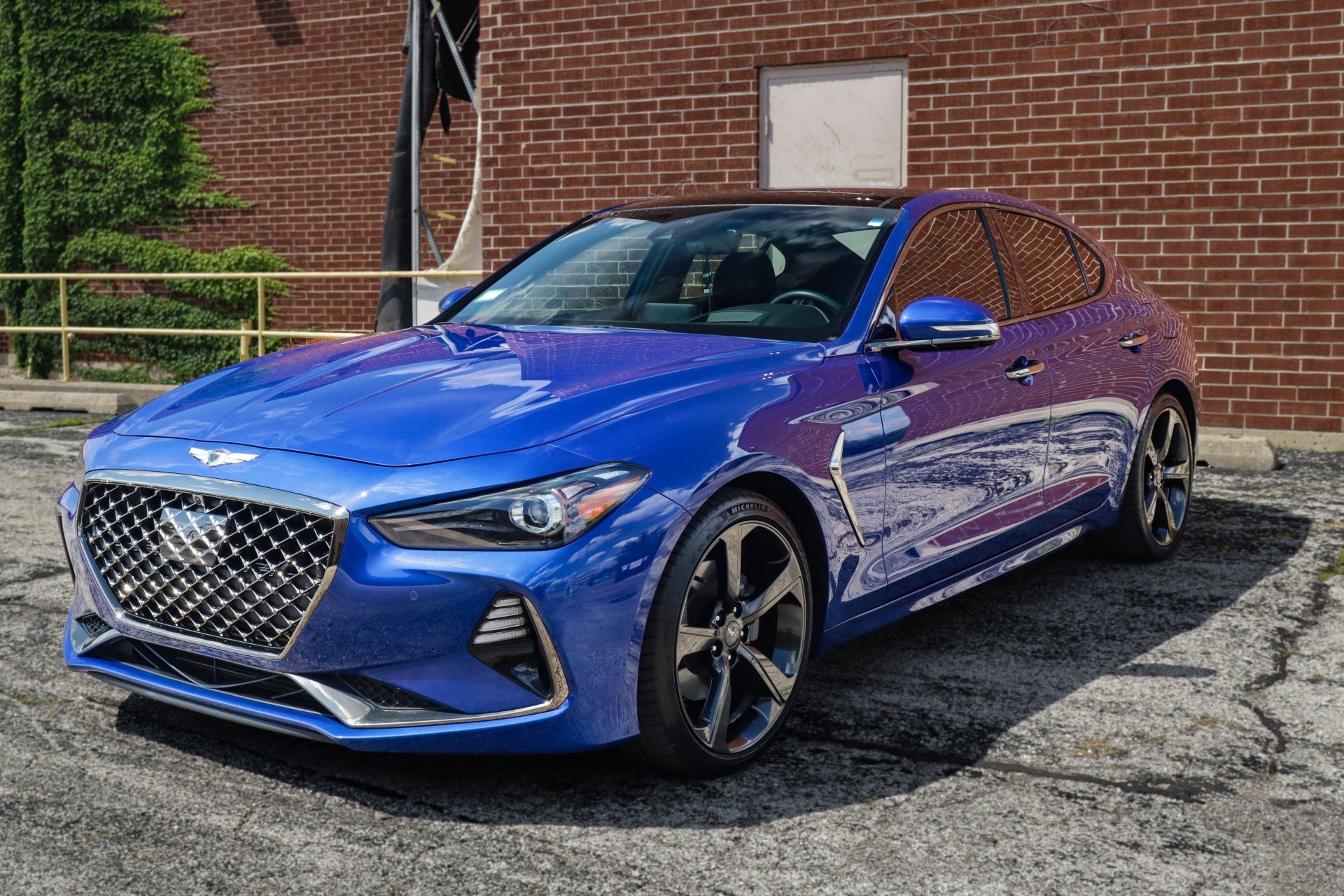 Blue Genesis G70 parked in front of a brick building.