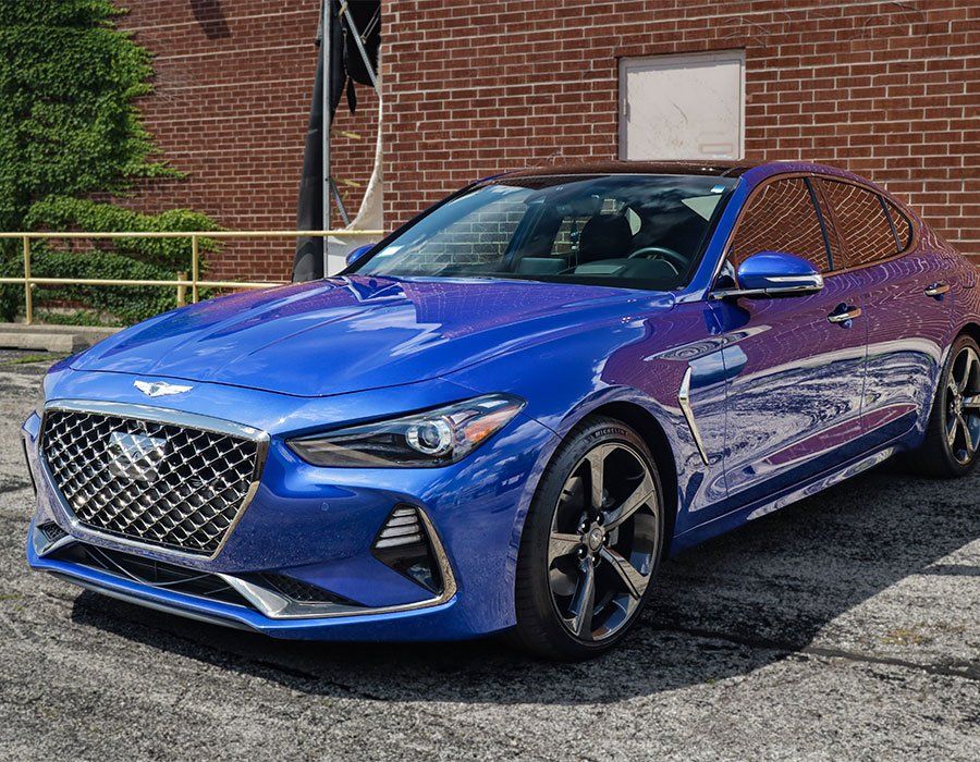A blue hyundai genesis is parked in front of a brick building.