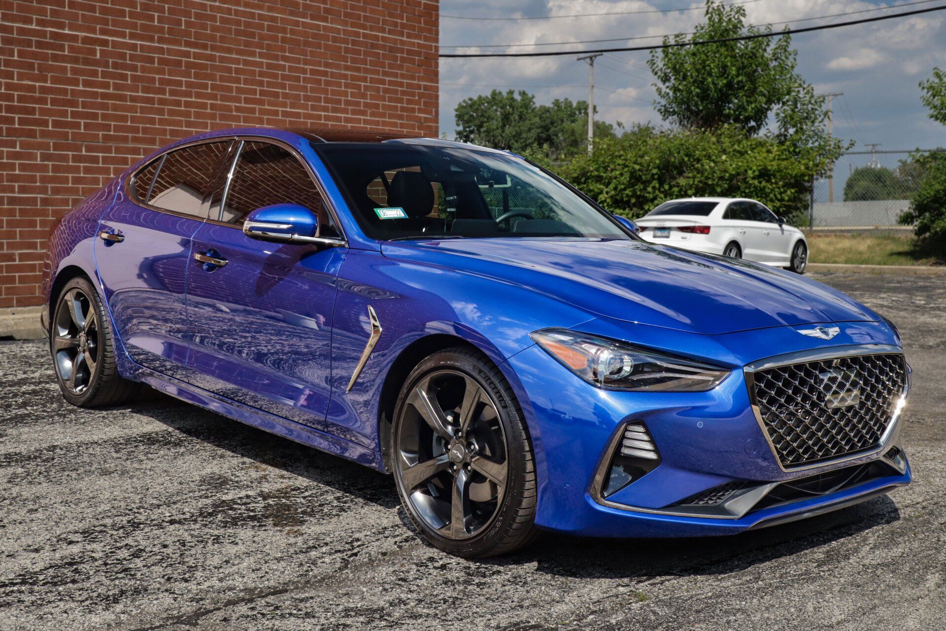 Blue Genesis G70 sedan parked in front of a brick building on a sunny day.