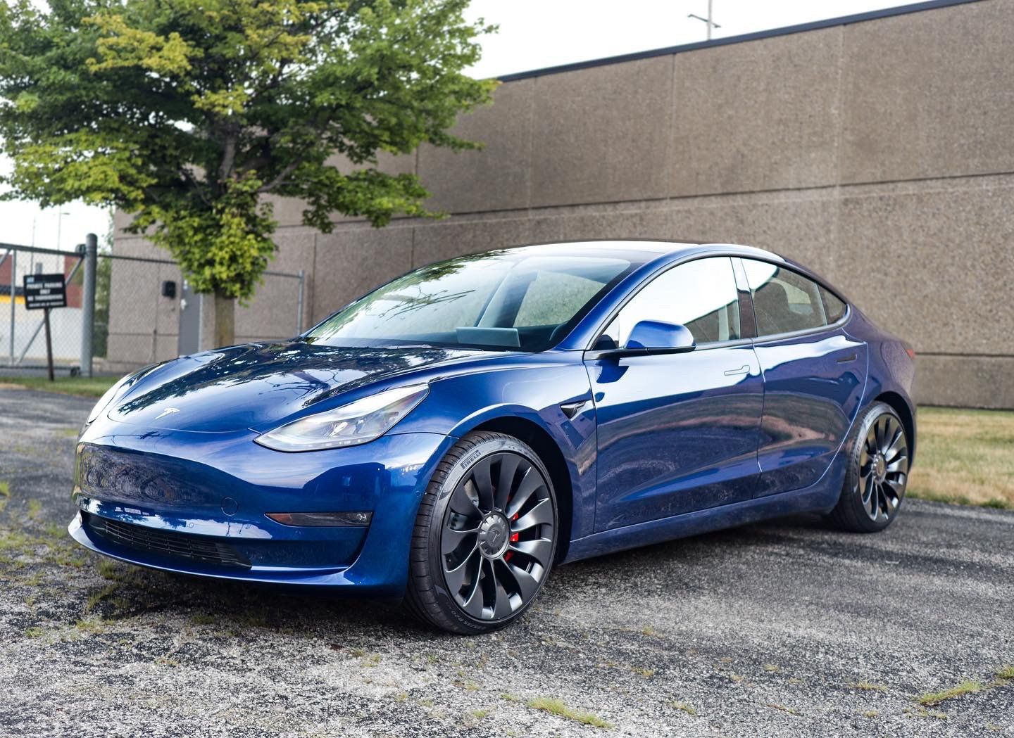 Blue Tesla Model 3 parked outdoors in front of a building.