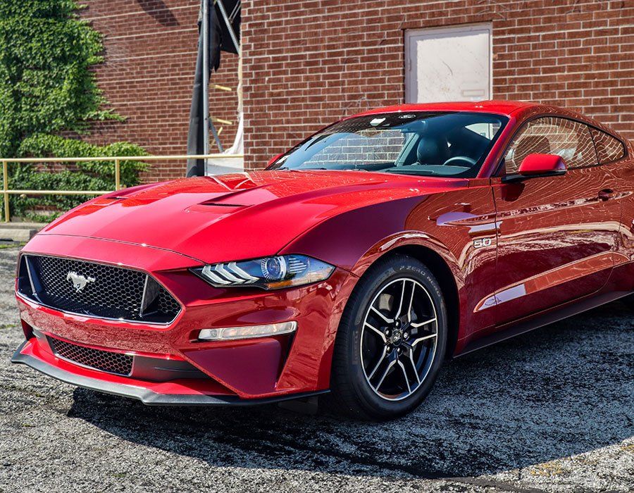 A red ford mustang is parked in front of a brick building.