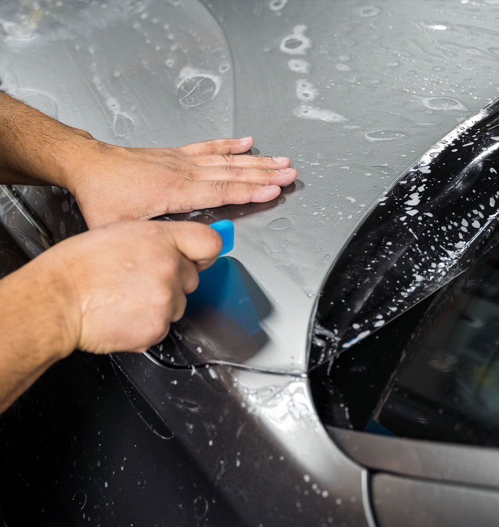 Person applying protective film to a car's body, using a smoothing tool.