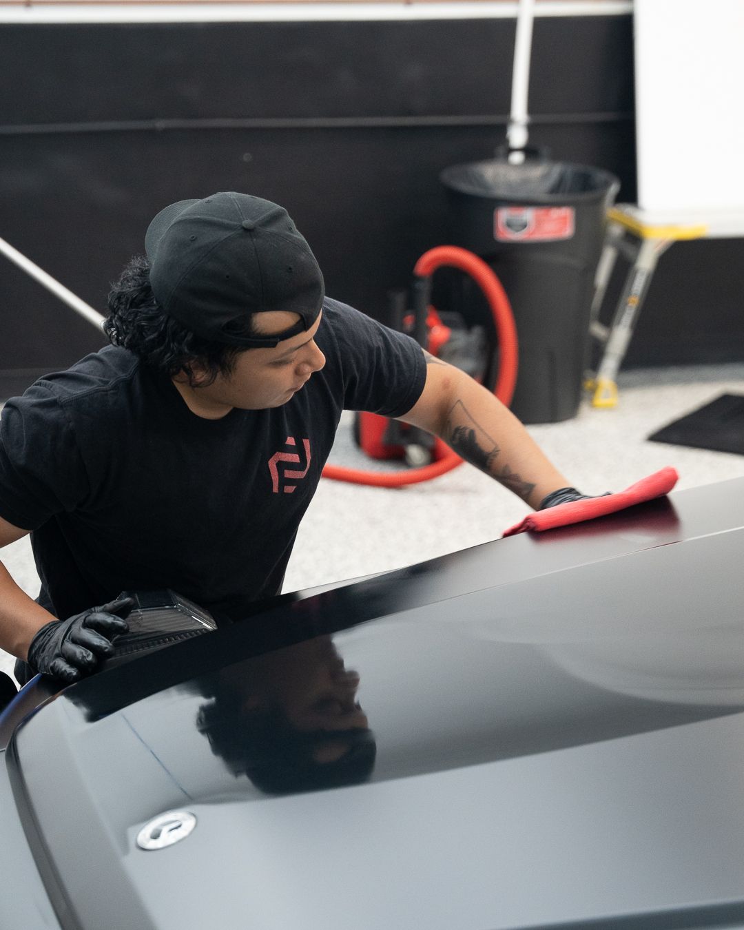 Person wiping a gray car hood with a red cloth in an auto detailing shop