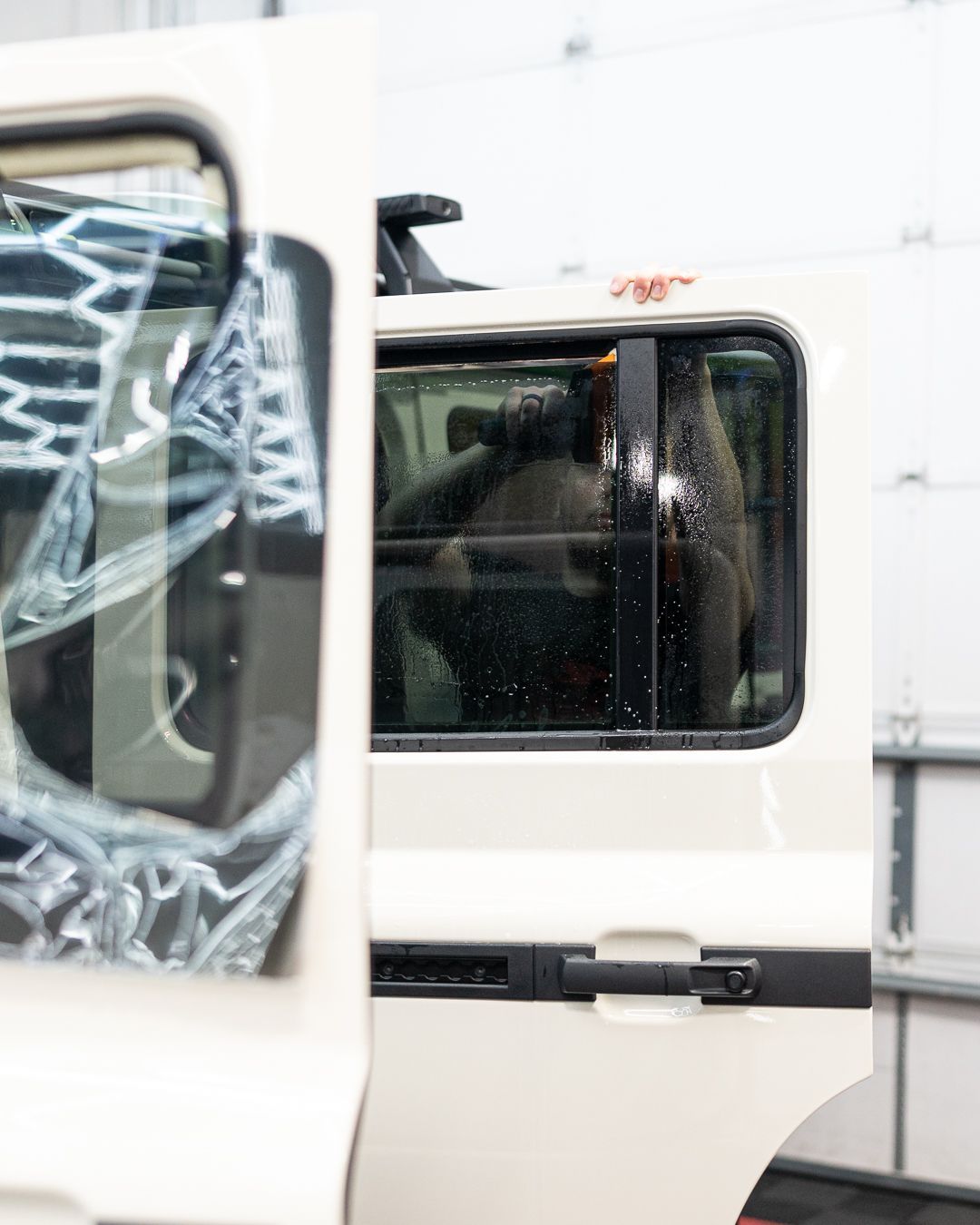 Open white van door with dark tinted window and plastic-covered interior in a garage