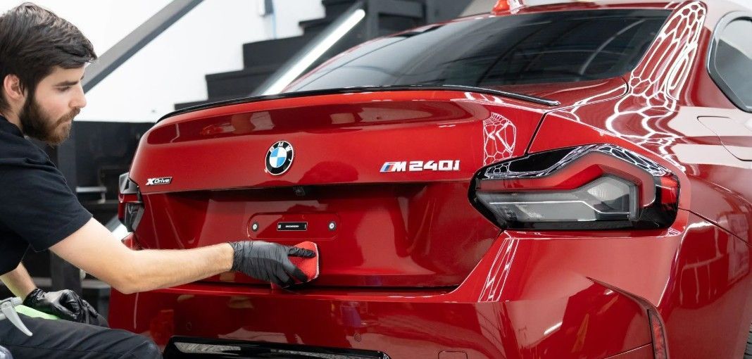 Mechanic polishing the rear of a red BMW M240i in a garage