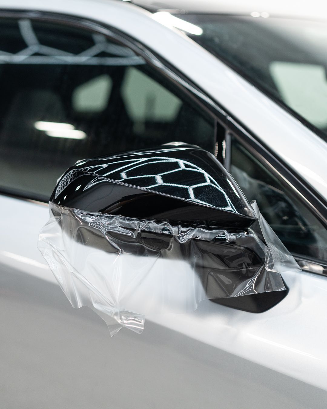Black car side mirror wrapped in protective plastic on a white vehicle