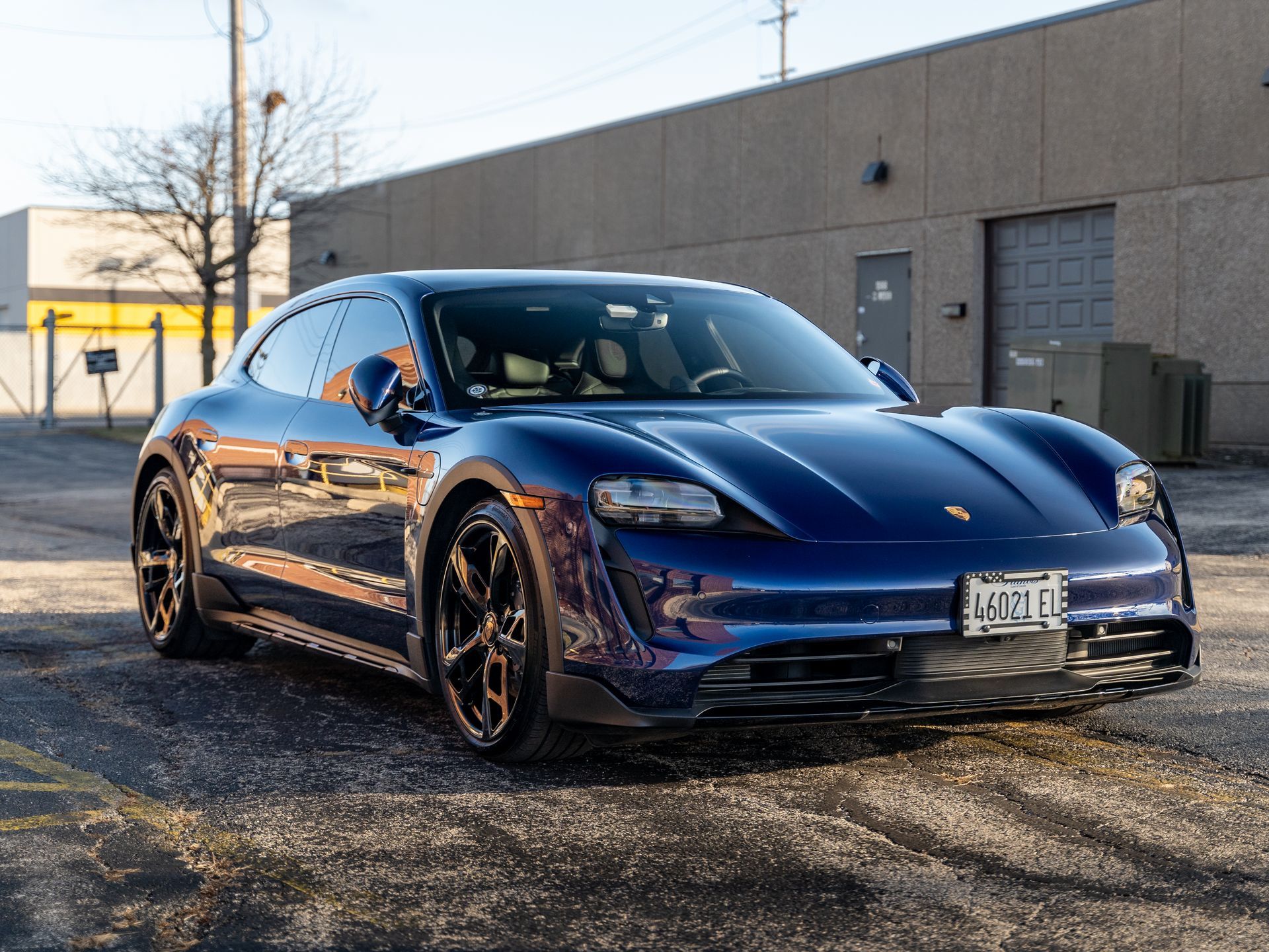 A blue porsche taycan is parked in front of a building.