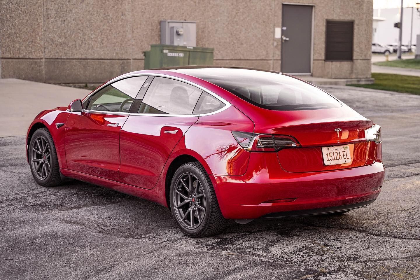 Red Tesla sedan parked beside a beige building on wet pavement