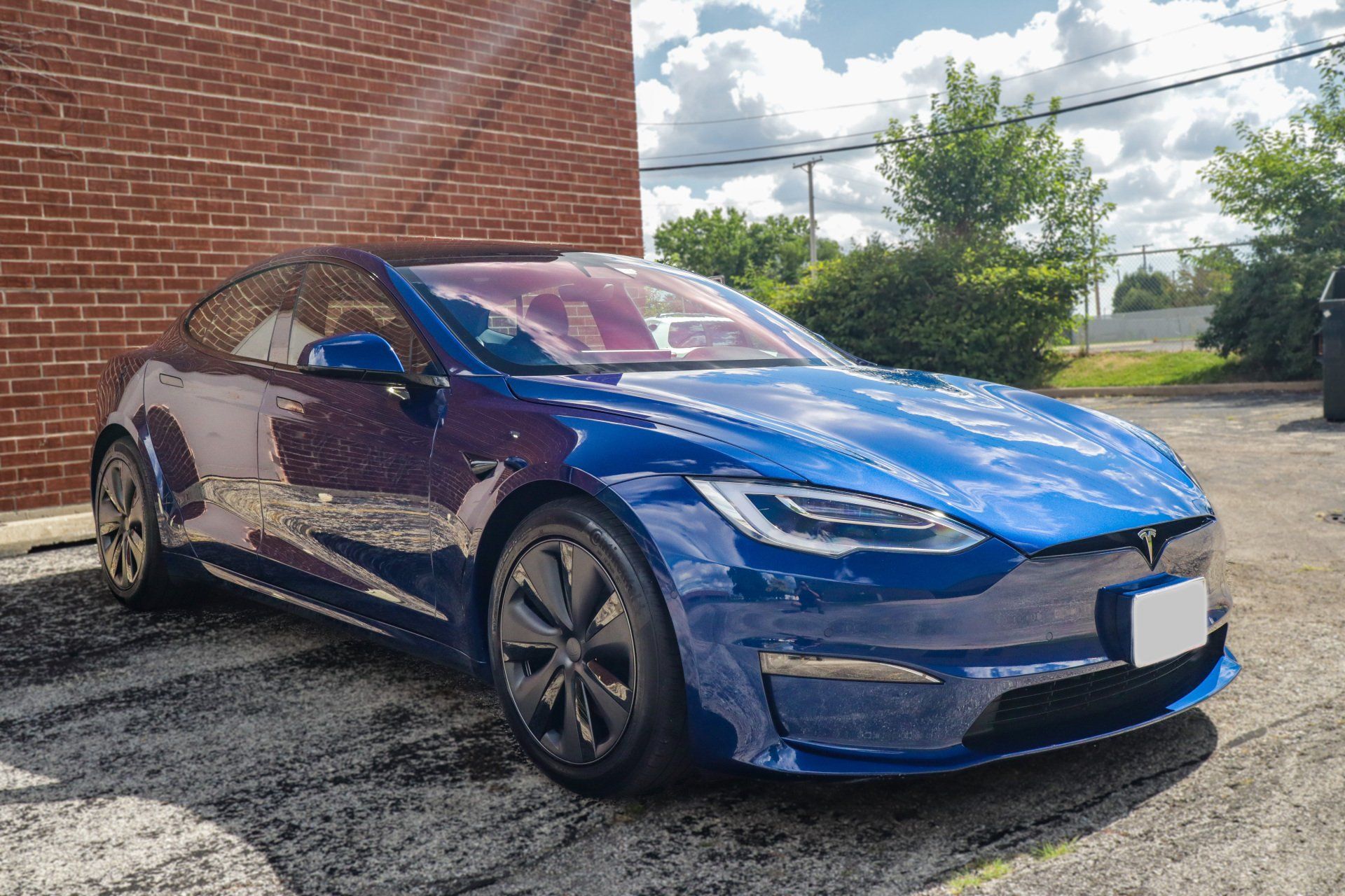 A blue tesla model s is parked in front of a brick building.