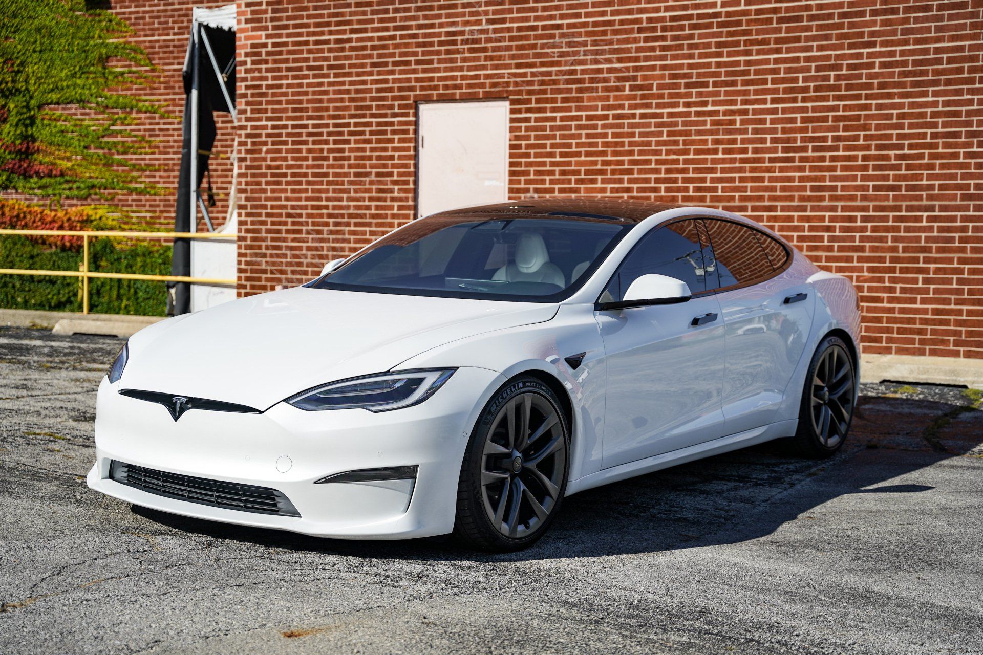 A white tesla model s is parked in front of a brick building.