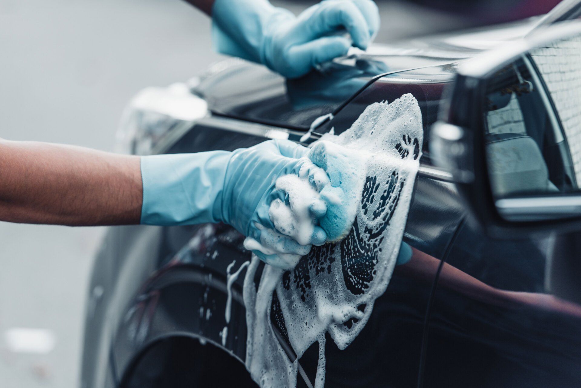 A person is washing a car with a towel and gloves.