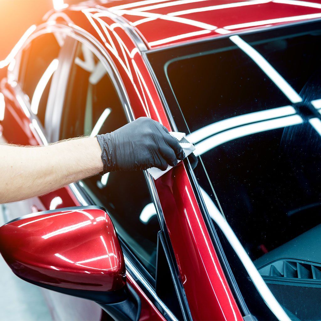 A man wearing black gloves is cleaning the windshield of a red car.