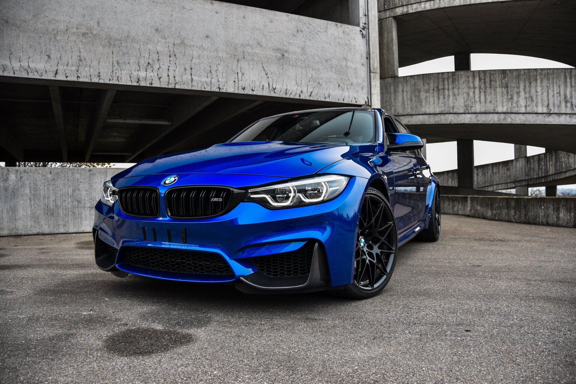 A blue bmw m3 is parked in front of a concrete building.