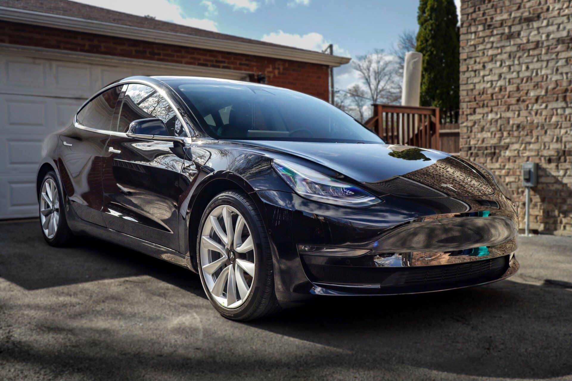 A black tesla model 3 is parked in front of a garage door.