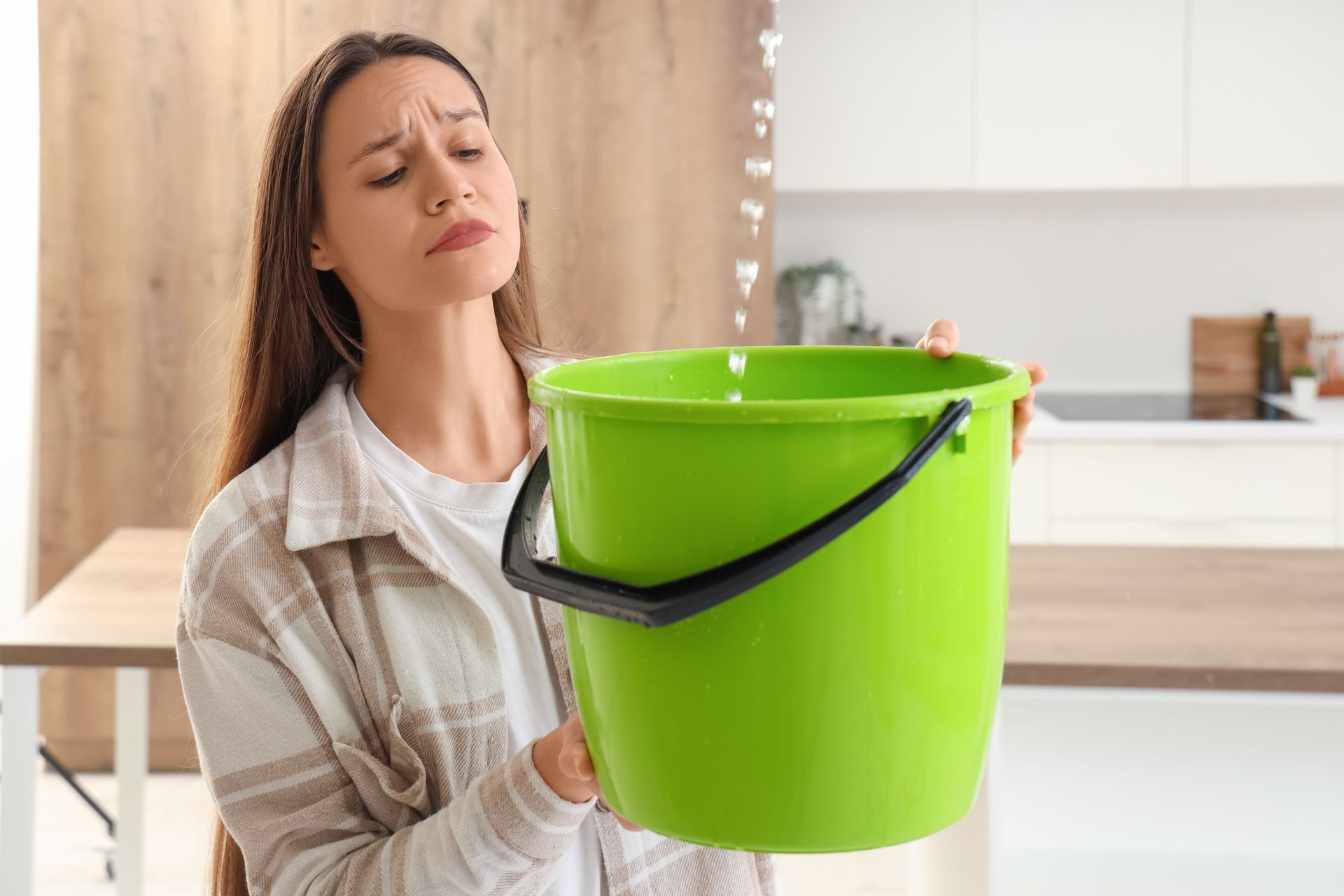 A person holding a bucket, catching a dripping ceiling leak, addressing a water damage issue.