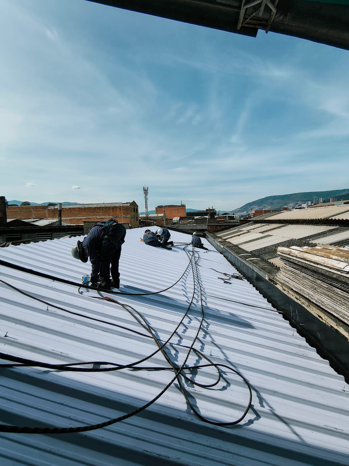 Un trabajador en un tejado utilizando una sierra circular cerca del canalón, con unos planos sobre un andamio debajo.