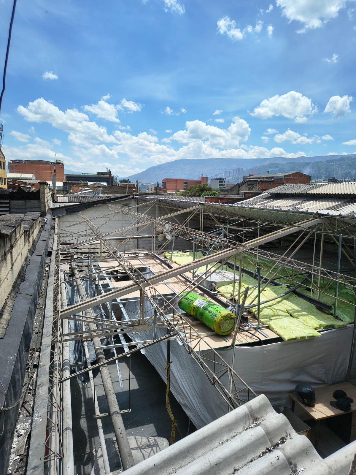 Obreros de la construcción con chalecos naranjas pintan una pared gris con rodillos en una obra.