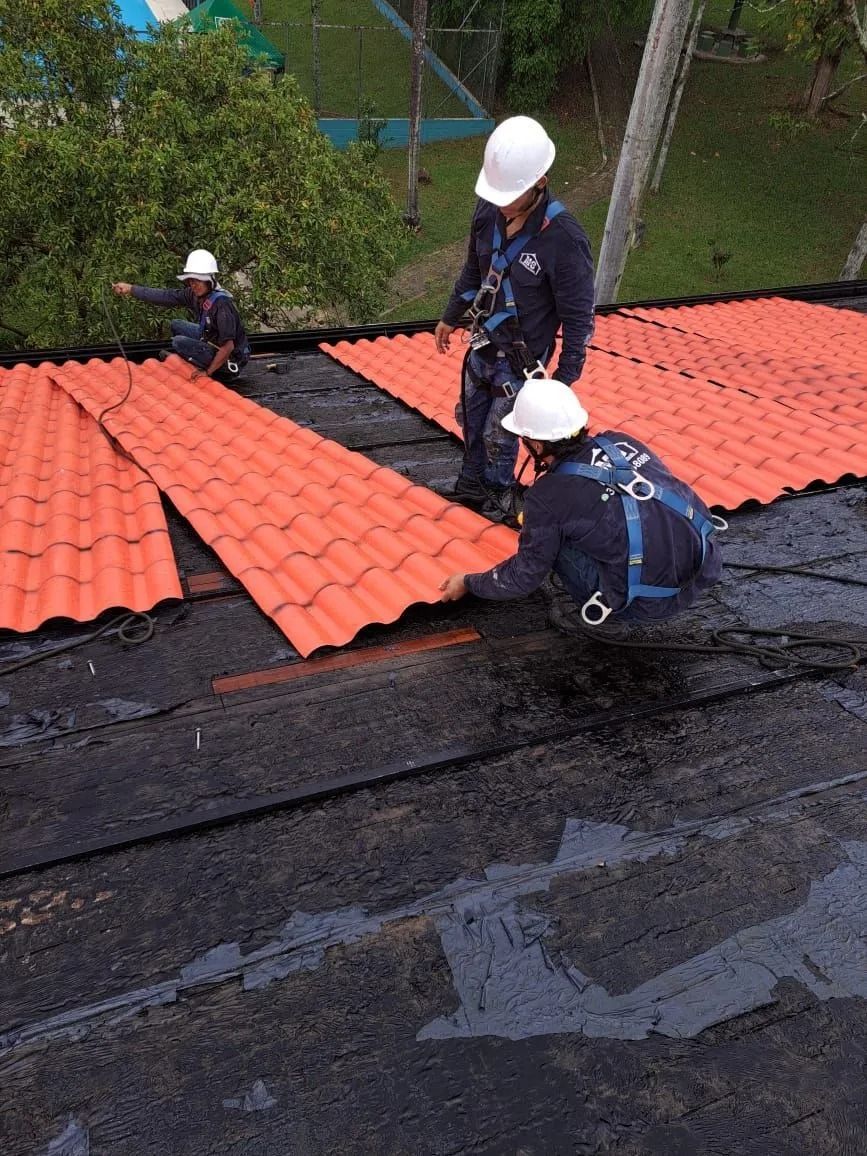 Trabajadores instalando paneles de techo rojos en un tejado negro empinado al aire libre.