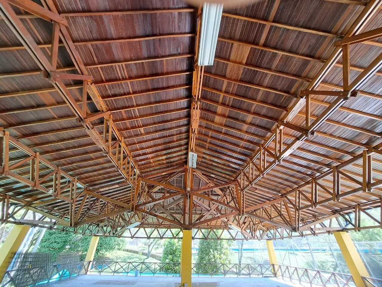 Pabellón al aire libre con techo alto de madera y vigas de soporte amarillas.