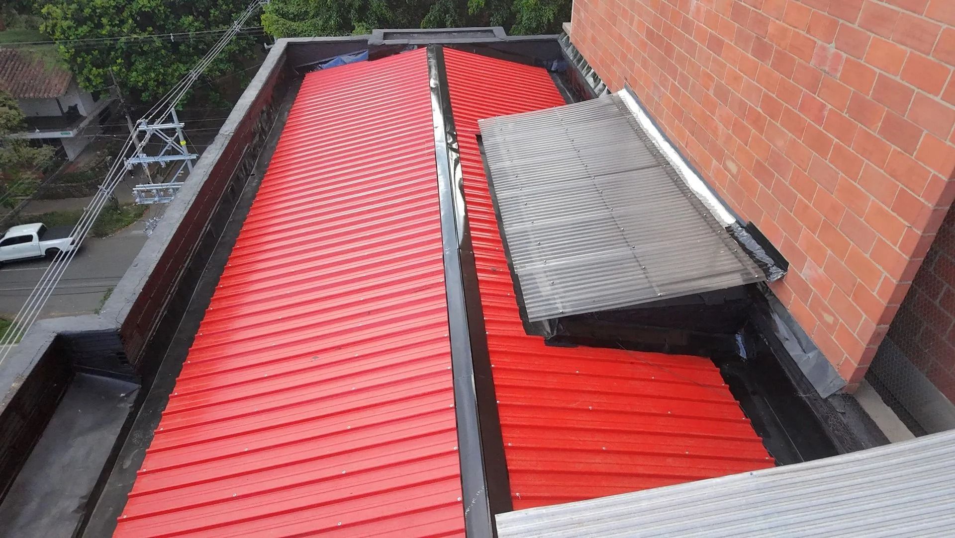 Techo de metal rojo con una lámina gris parcialmente levantada junto a una pared de ladrillos y una pasarela en la azotea.