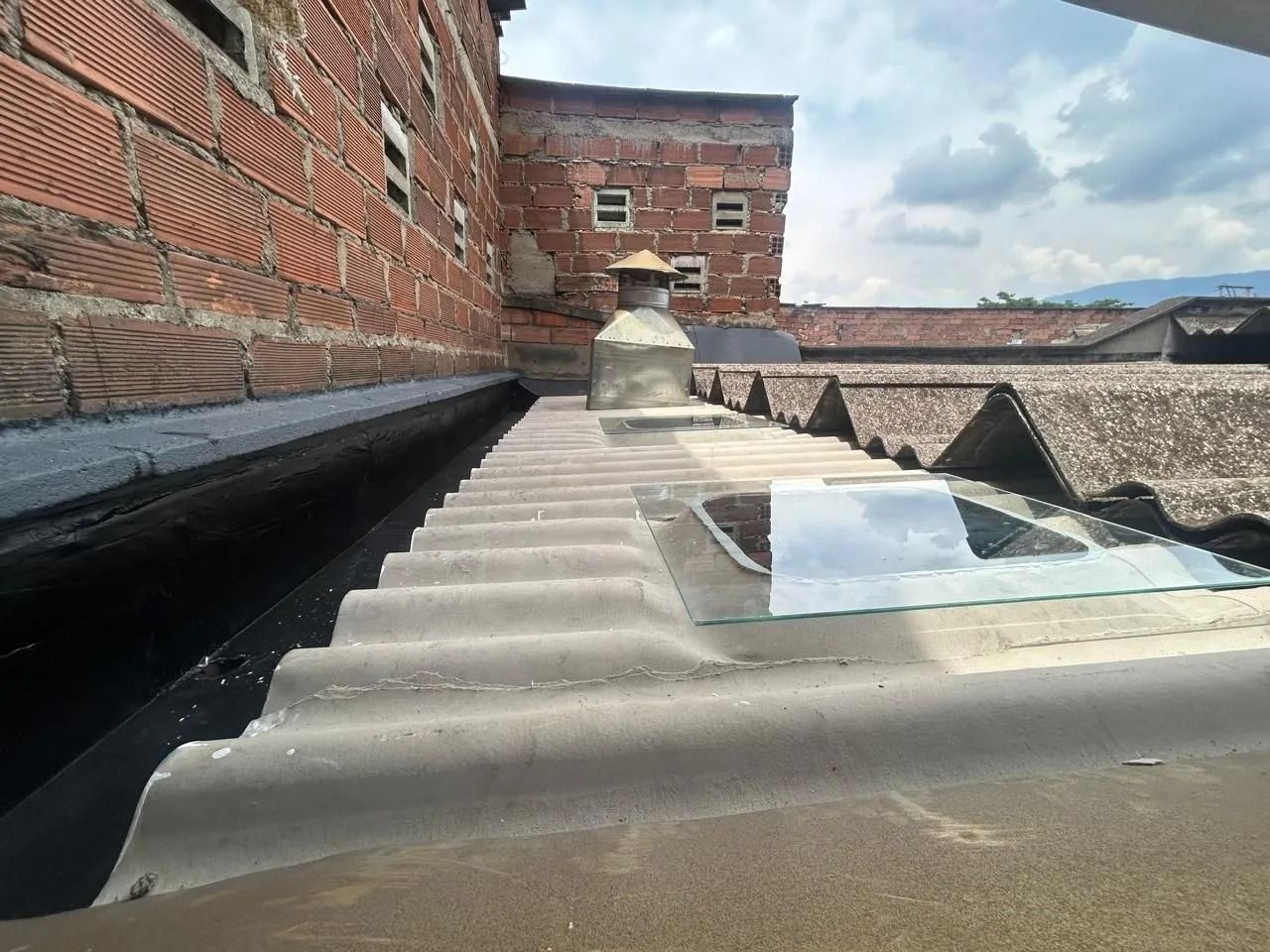 Azotea con paneles corrugados junto a una pared de ladrillo y una pequeña claraboya bajo un cielo nublado.