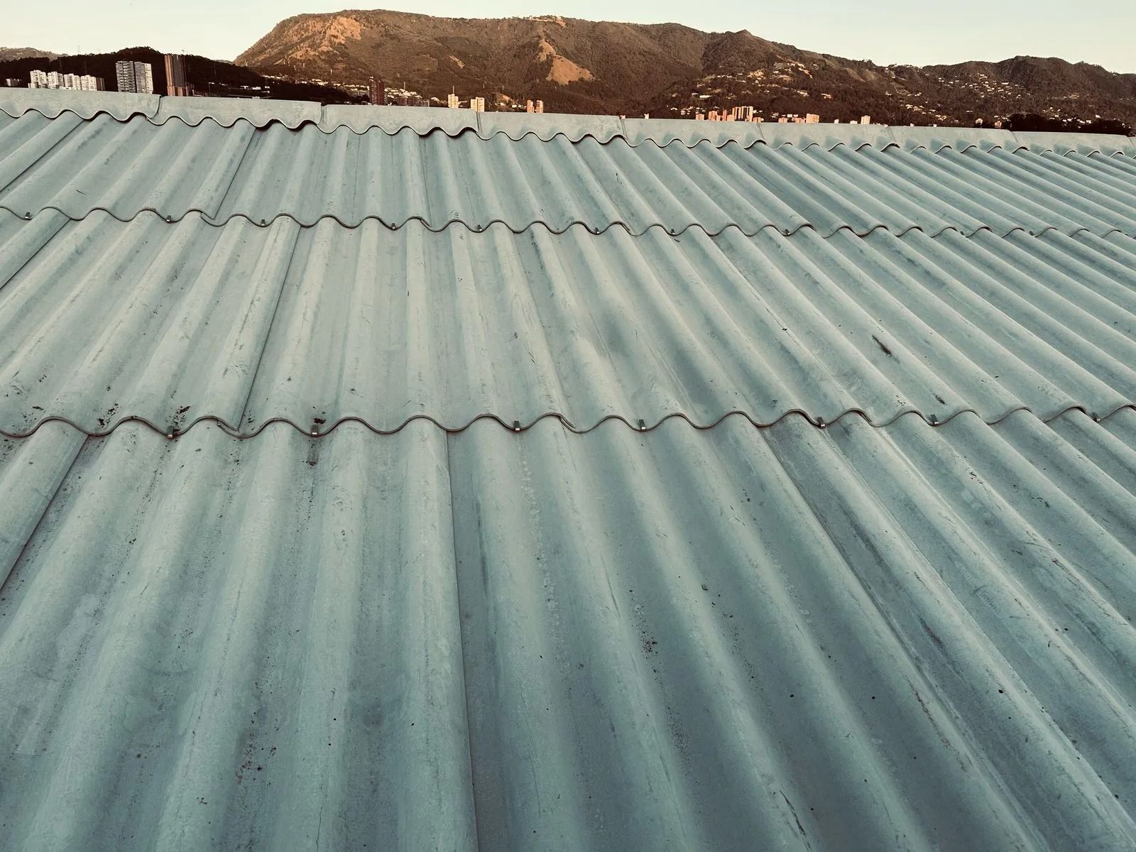 Techo de chapa ondulada azul con una ladera rocosa al fondo al atardecer.