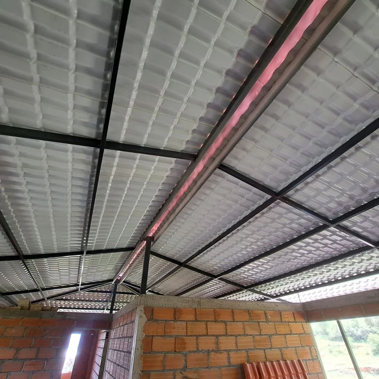 Vista interior de una cercha metálica sobre muros de ladrillo sin terminar en un edificio en construcción.