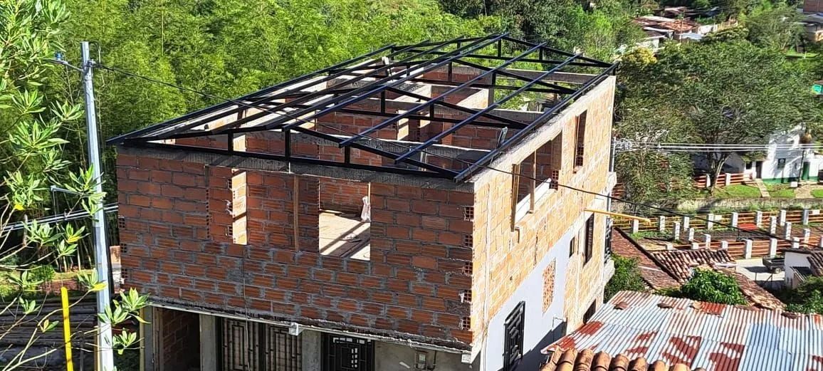 Casa de ladrillo parcialmente construida con estructura de acero a la vista en el tejado, en un barrio verde.