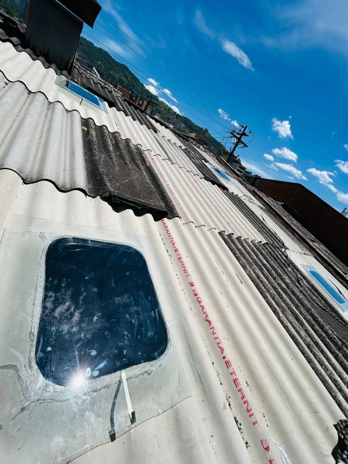 Vista inclinada de un techo de chapa ondulada con una pequeña claraboya y cielo azul.