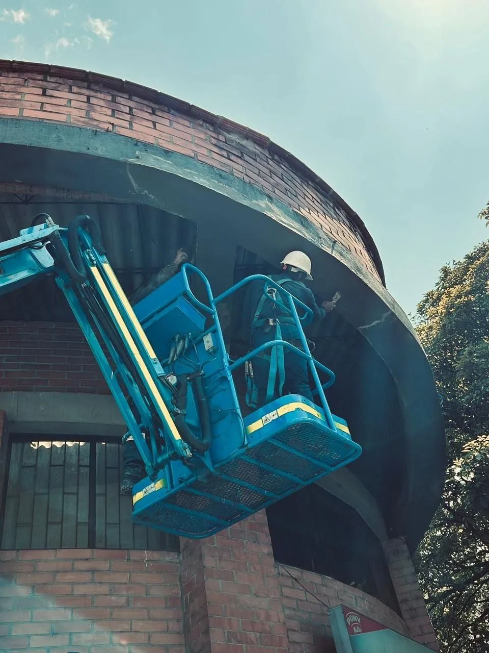 Una cesta elevadora de cerezas azul trabaja bajo el alero de un edificio de ladrillos.