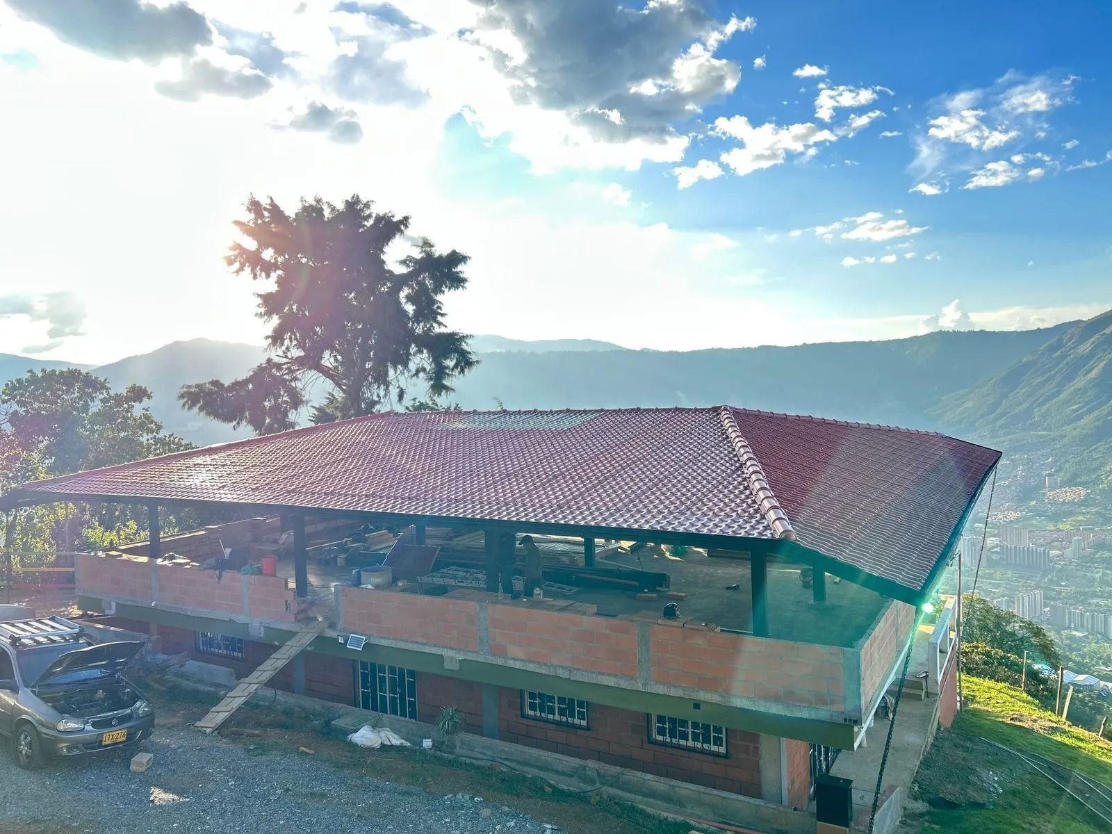 Casa rural con techo rojo en una ladera, con vistas a las montañas bajo un cielo azul brillante.