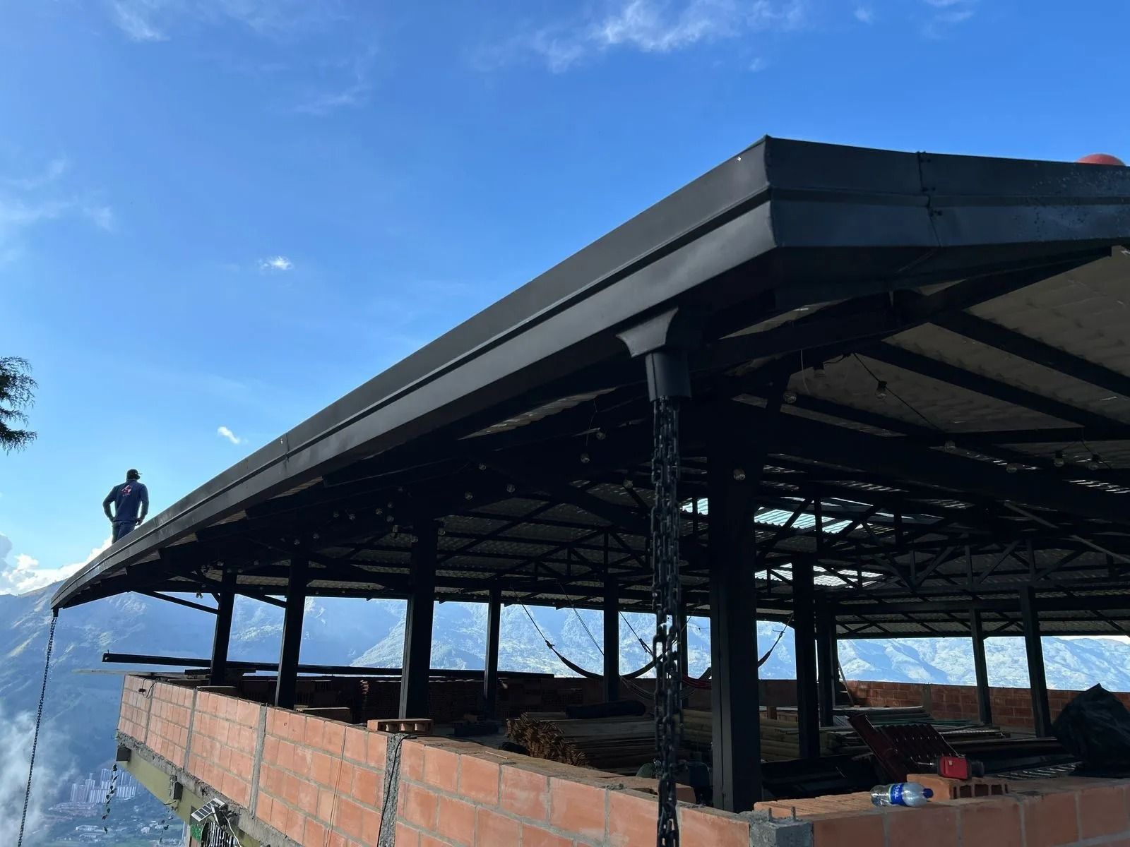 Pabellón abierto en construcción con pared de ladrillo, techo de metal y cielo azul.