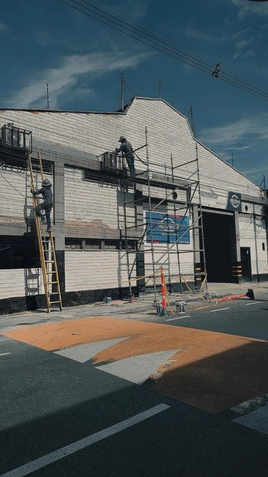 Edificio dañado con andamios y fachada tapiada junto a un cruce de calles bajo un cielo azul.