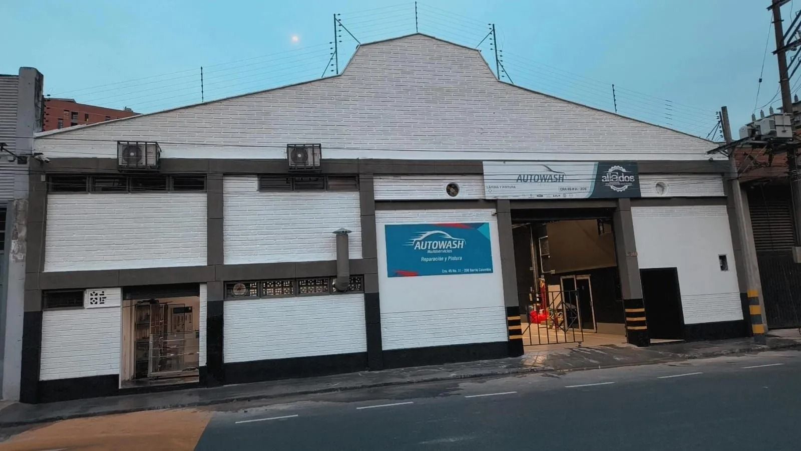 Edificio blanco con techo curvo y un letrero azul en la fachada, visto desde la calle.