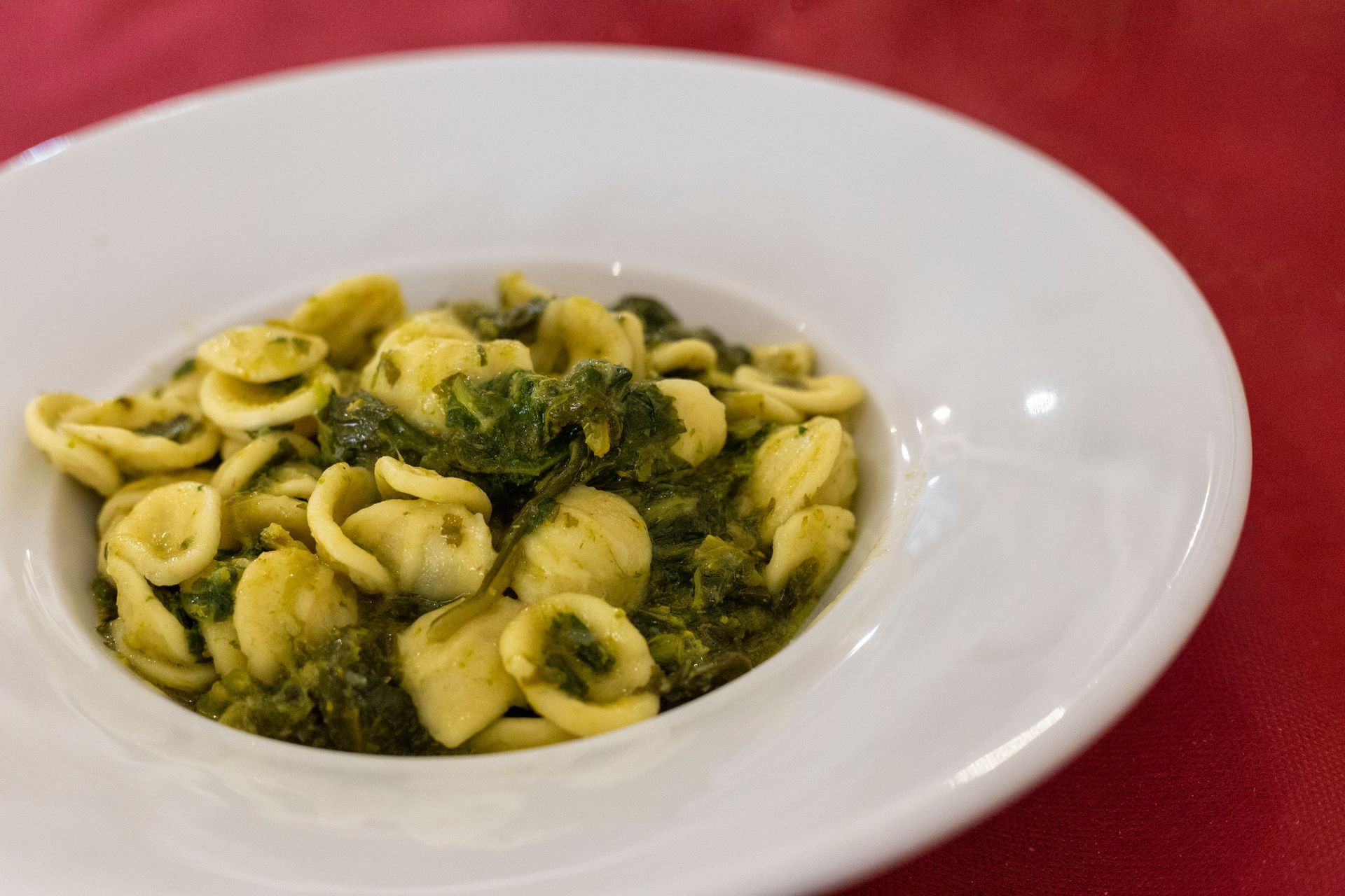 Pasta orecchiette con verdure in una ciotola bianca su una tovaglia rossa.