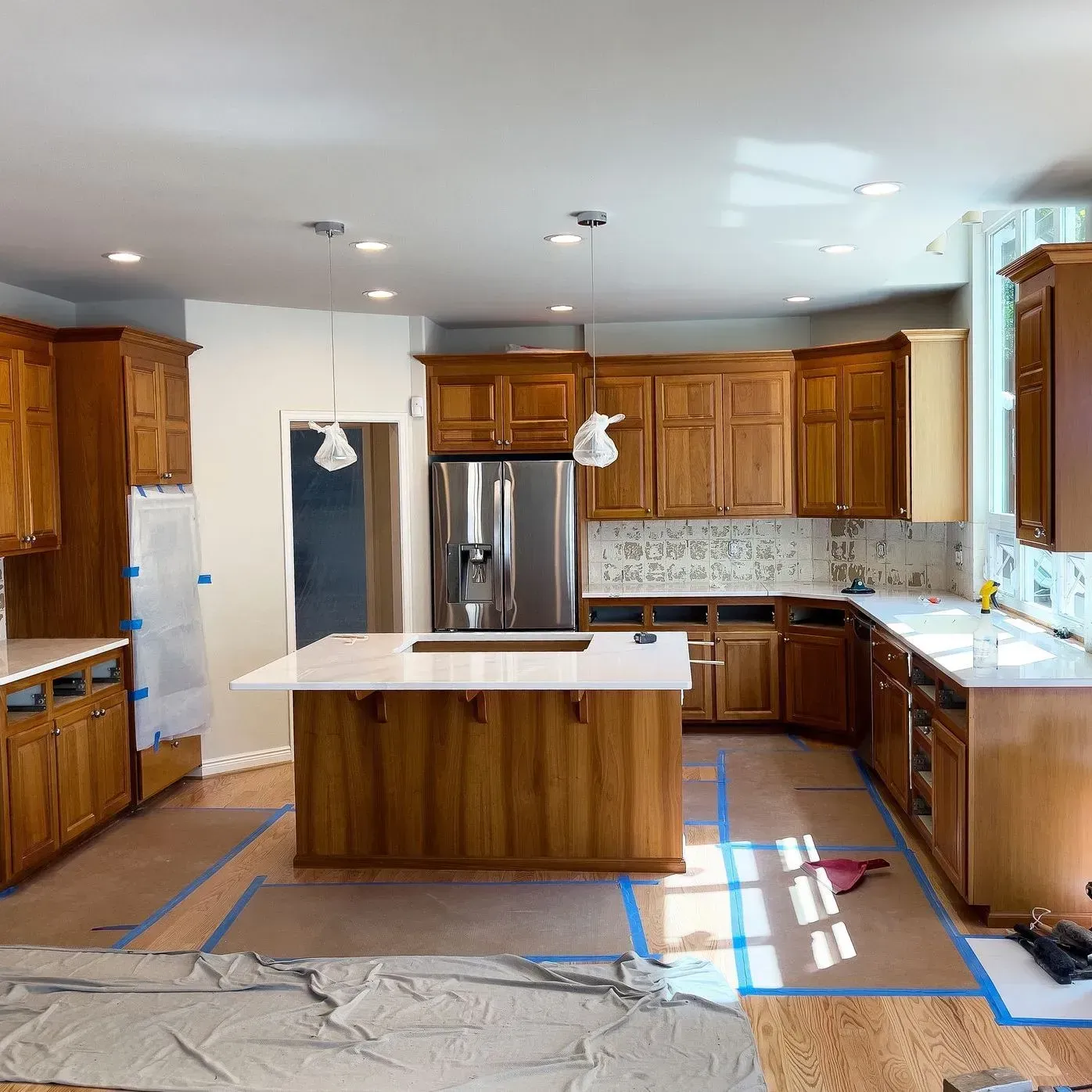 Kitchen under renovation with wood cabinets, island, stainless fridge, and taped-off floor area