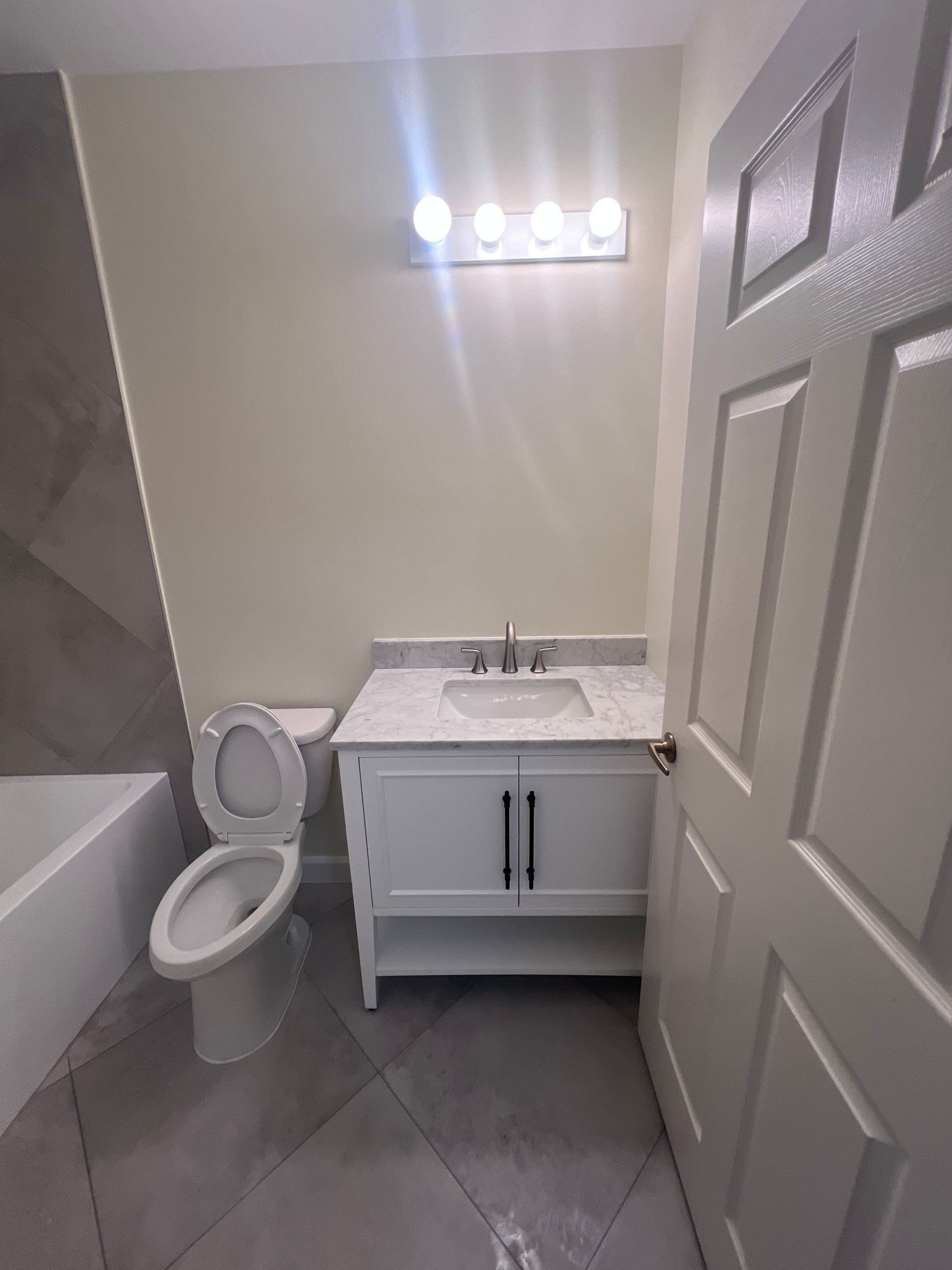 Small bathroom with toilet, white vanity sink, mirror lights, and gray tiled floor.